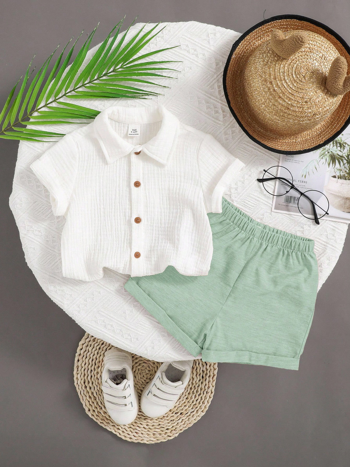 White shirt with buttons, green shorts, white sneakers, straw hat, and glasses on a gray background.